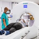 A person having a CT scan. They are lying on a bed attached to the CT scanner. The scanner is a large O shape, like a donut. The bed moves inside the hole to take the scan.