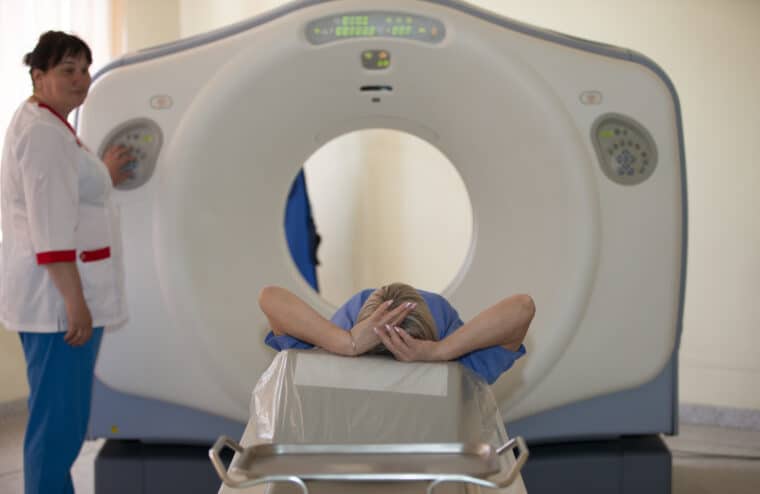 A person having an MRI scan. The scanner is a large machine with a hole in the middle. The person is lying down with hands on their head. The bed moves into the hole for the scan.